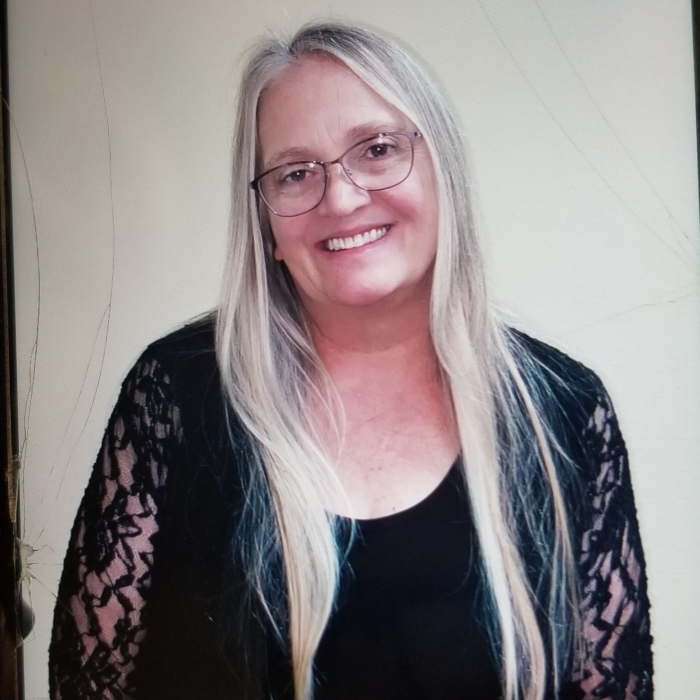Woman with straight, blonde hair wearing a black blouse in front of a white wall.