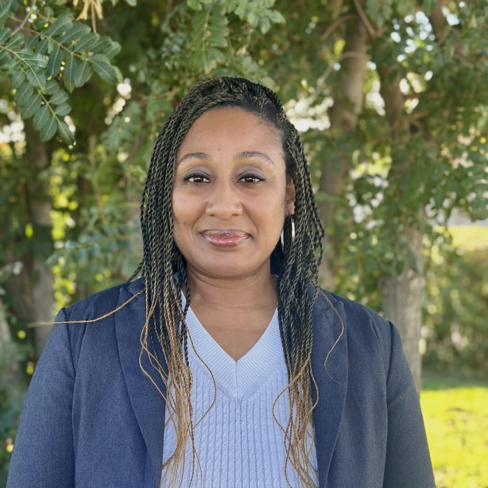 Woman with braids wearing white blouse and blue blazer with trees in background