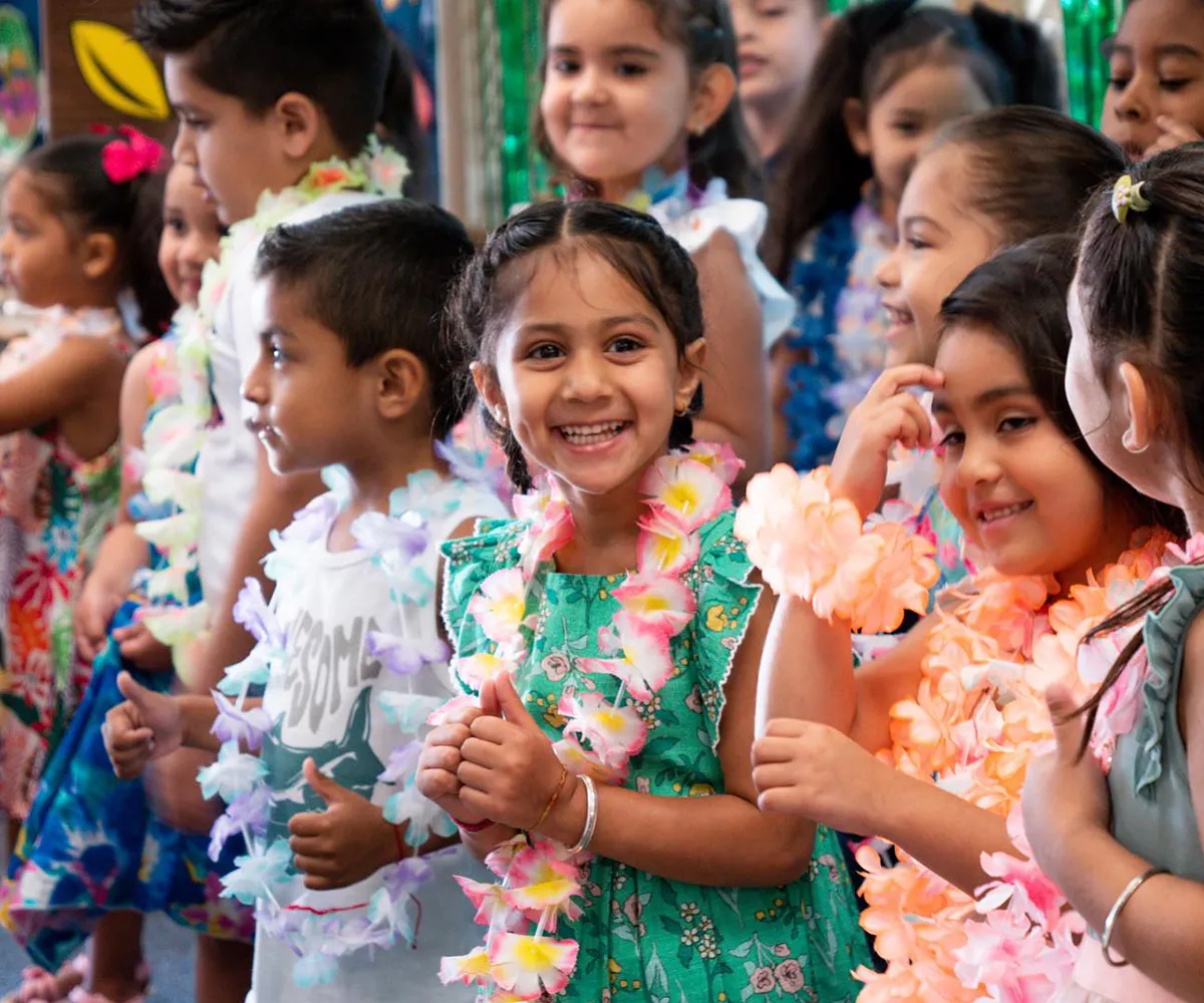 A group of smiling children in colorful leis and dresses stand together, enjoying a festive celebration.