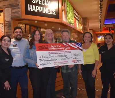 Six people at a restaurant hold a large $2,000 donation check for Family Services Associates.
